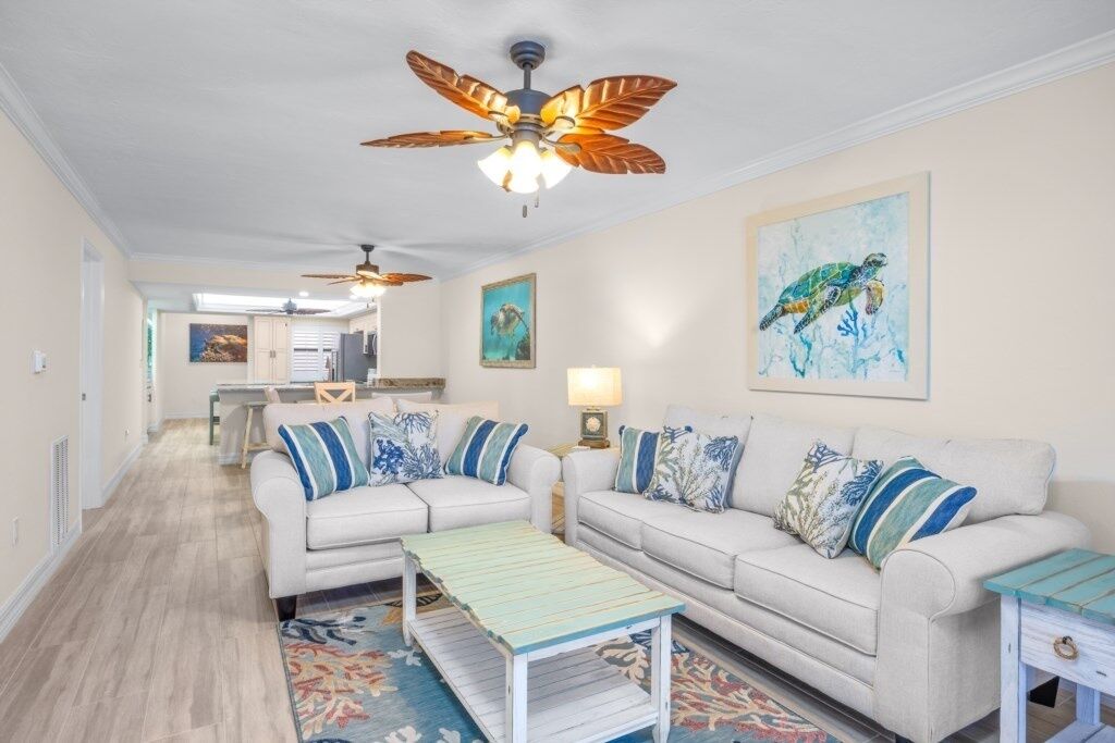 A spacious living room with two white sofas, a wooden coffee table, and a ceiling fan.