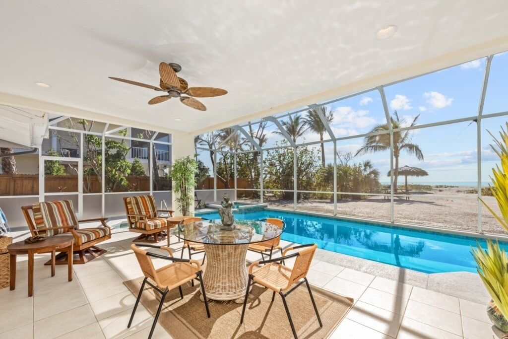 A poolside area with wicker furniture, a ceiling fan, and a view of the beach.