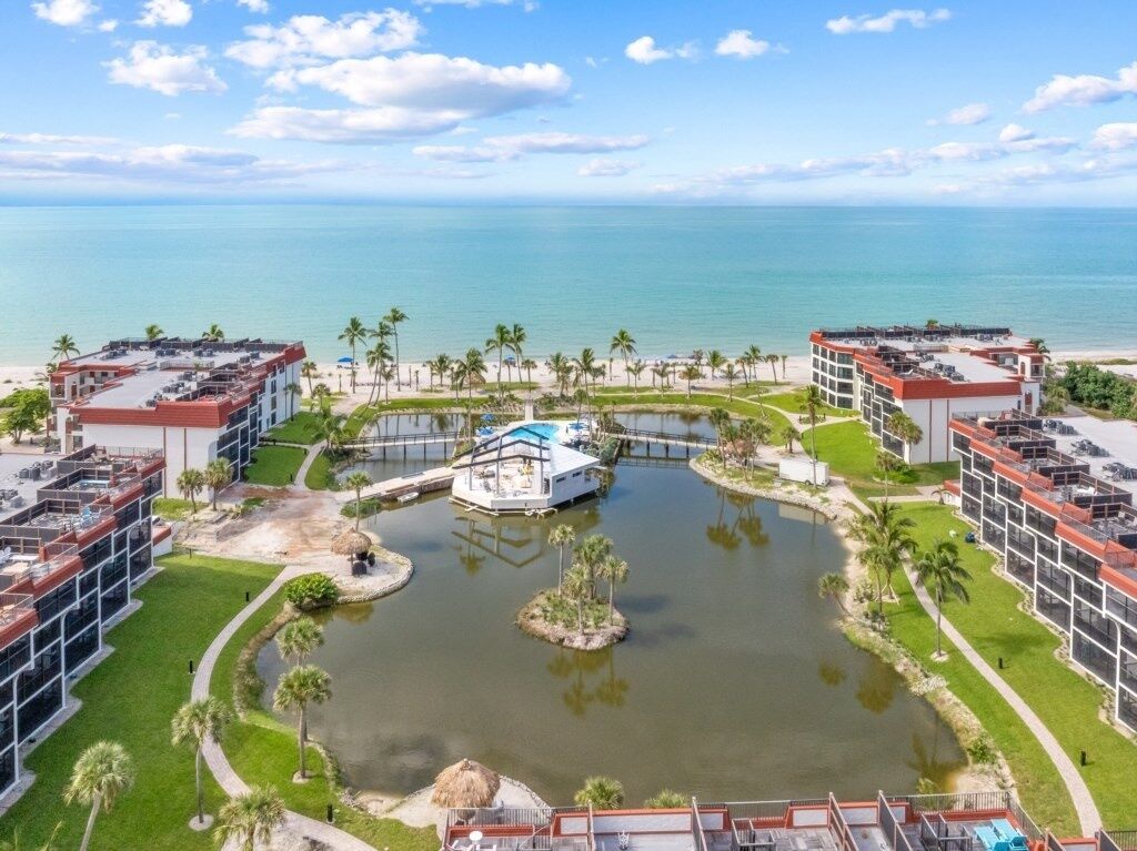 A resort with a central water feature, connected to a beach area, surrounded by modern buildings with balconies.