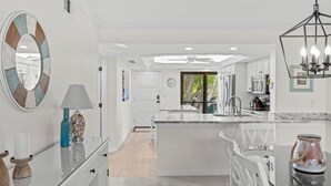 A modern kitchen with white cabinetry, a central island, and a dining area with white chairs. - Pointe Santo D27 2 Bedroom Condo (Sanibel)