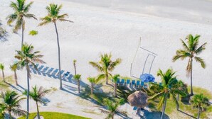 An aerial view of a beach with palm trees, a thatched-roof hut, and a row of beach chairs and umbrellas. - Pointe Santo D27 2 Bedroom Condo (Sanibel)
