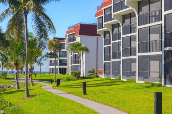 A modern hotel with multiple floors, balconies, and a well-maintained lawn with palm trees. - Pointe Santo E44 3 Bedroom Condo (Sanibel)