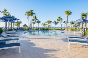 A poolside area with lounge chairs and umbrellas, palm trees, and a view of the ocean. - Pointe Santo D35 2 Bedroom Condo (Sanibel)