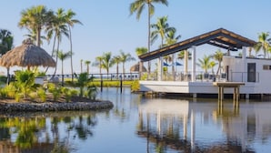 A modern resort with a pool, palm trees, and a thatched-roof structure. - Pointe Santo D35 2 Bedroom Condo (Sanibel)