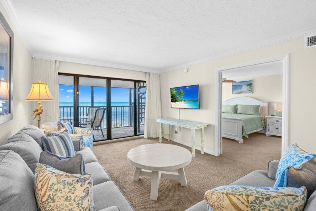 A hotel room with a balcony, a TV, a bed, and a seating area with a table.