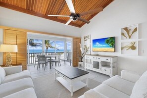 A spacious living area with a ceiling fan, a television, and a view of the beach through large windows. - South Seas Beach Villa 2538 3 Bedroom Condo (Captiva)