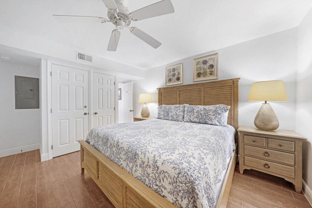Une chambre à coucher avec un lit, une table de chevet, un ventilateur de plafond et une porte.