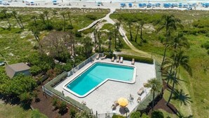 Ett flygbildsbild av ett semesterområde med en swimmingpool, tillgång till stranden och palmer.