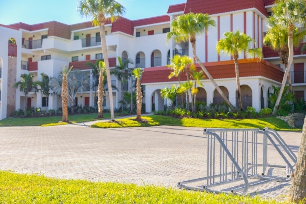 A multi-story hotel with a red and white facade, palm trees, and a paved courtyard.