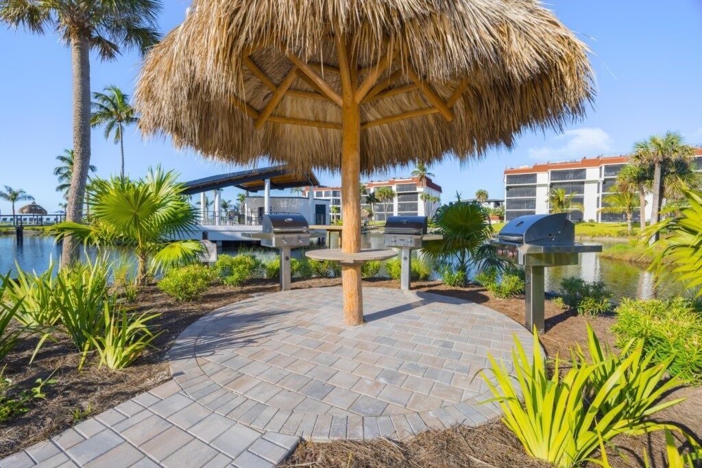 Un área de patio con sombrilla de paja, parrillas al aire libre y vista a la piscina.