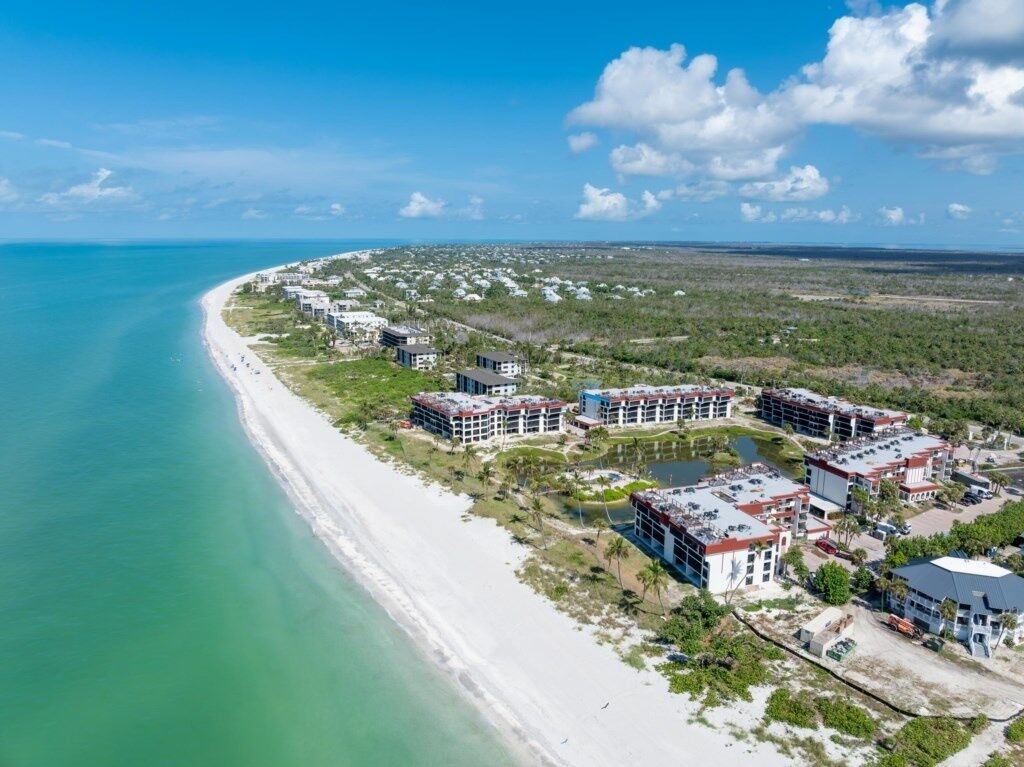 Une station balnéaire dotée de villas en bord de mer, d’une plage de sable fin et d’un ciel bleu azur.