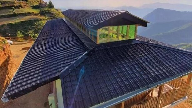 A two-story building with a steeply pitched roof, situated on a hillside with a view of distant mountains. - VEDA INN (Kalsi)