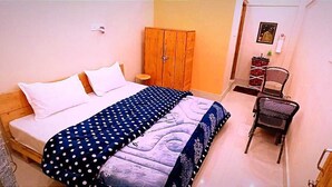 A bedroom with a bed, a wardrobe, a chair, and a small table. - VEDA INN (Kalsi)