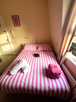 Una habitación pequeña con una cama individual, una colcha a rayas, un teléfono en la mesita de noche y una ventana con cortinas.