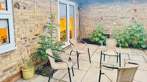 Ein Backsteinhaus mit Terrasse, ausgestattet mit Korbstühlen und Topfpflanzen.