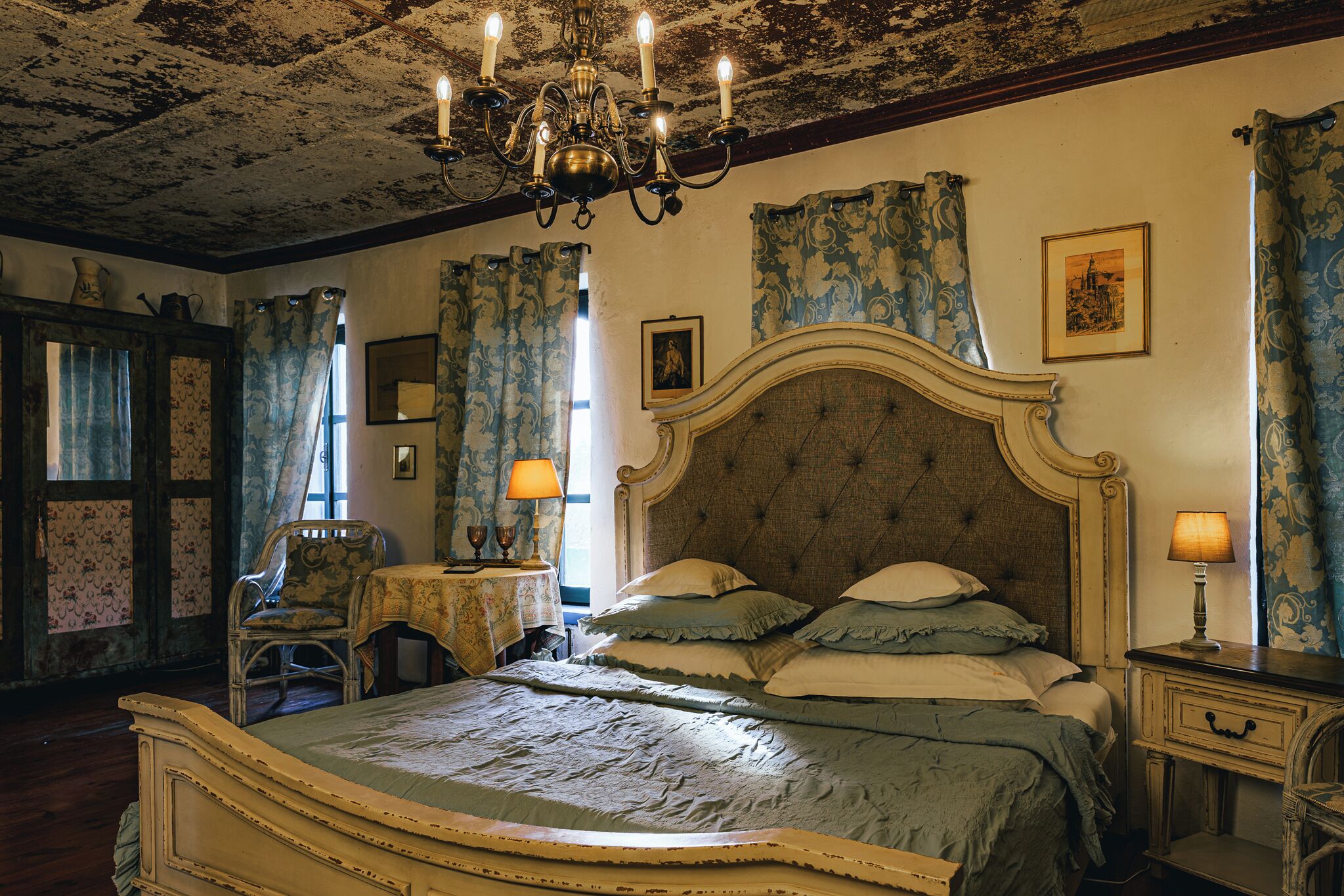A bedroom with a large bed, a chandelier, and a classic design.