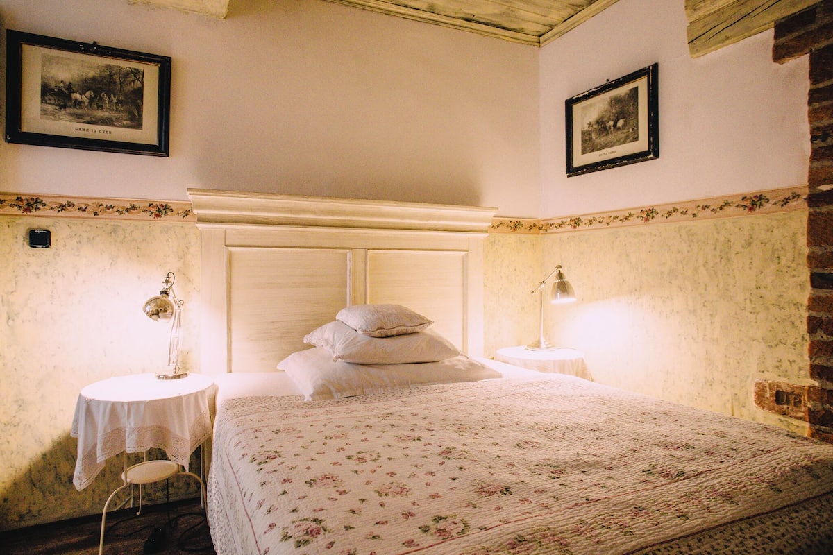 A bedroom with a bed, two bedside tables, a lamp, and framed pictures on the walls.
