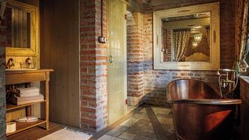 A bathroom with a wooden vanity, a large mirror, a copper bathtub, and a brick wall.