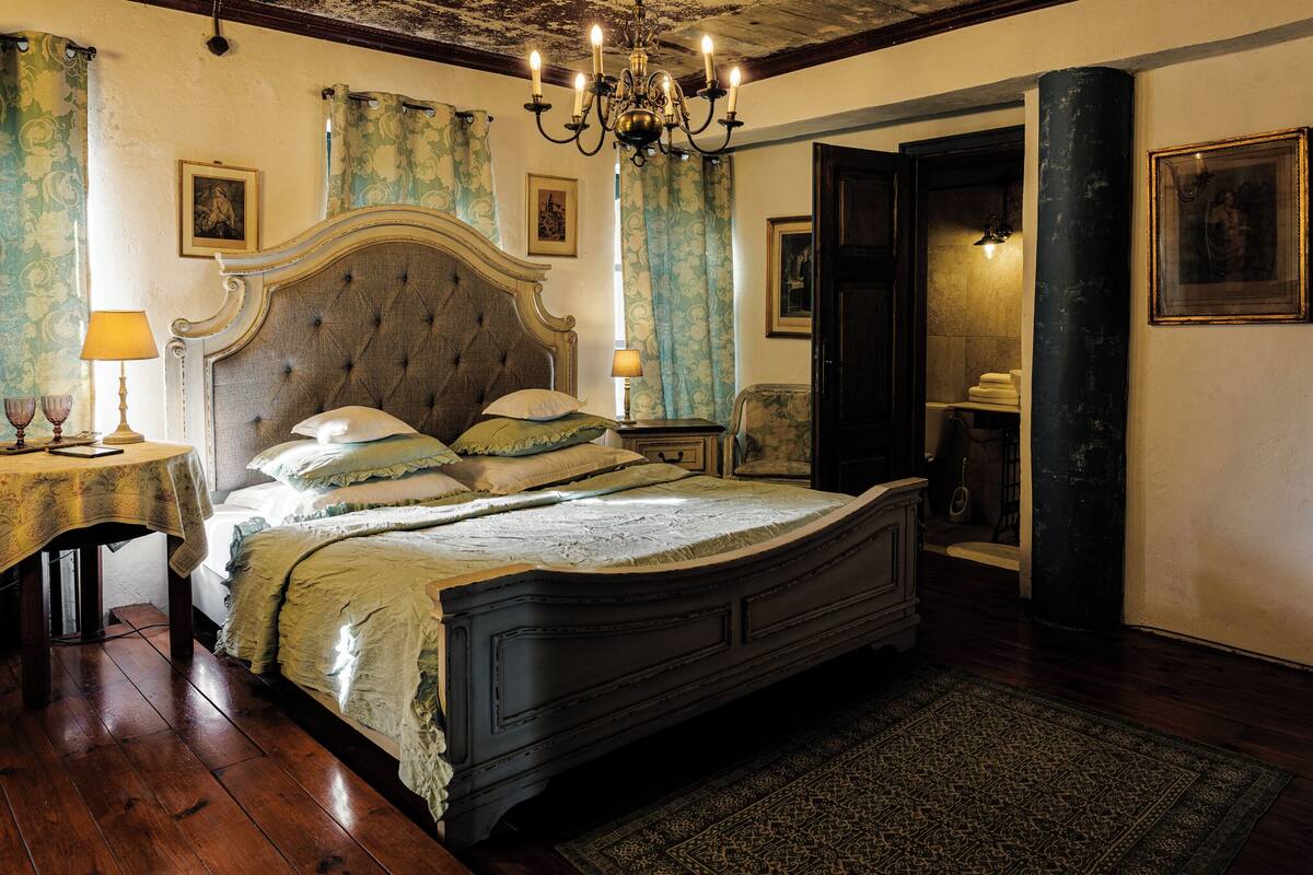 A classic bedroom with a large bed, a chandelier, and a wooden floor.