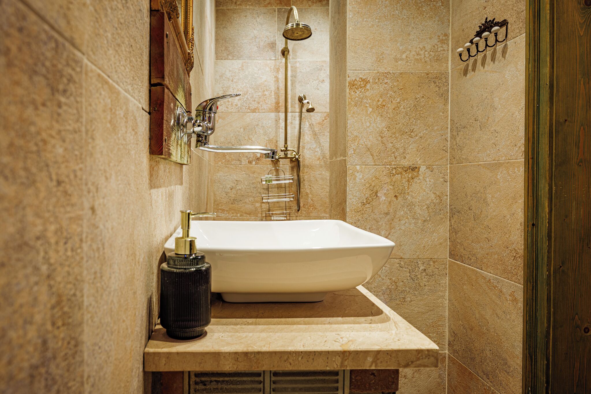 A bathroom with a white sink, a handheld showerhead, and a wall-mounted light fixture.