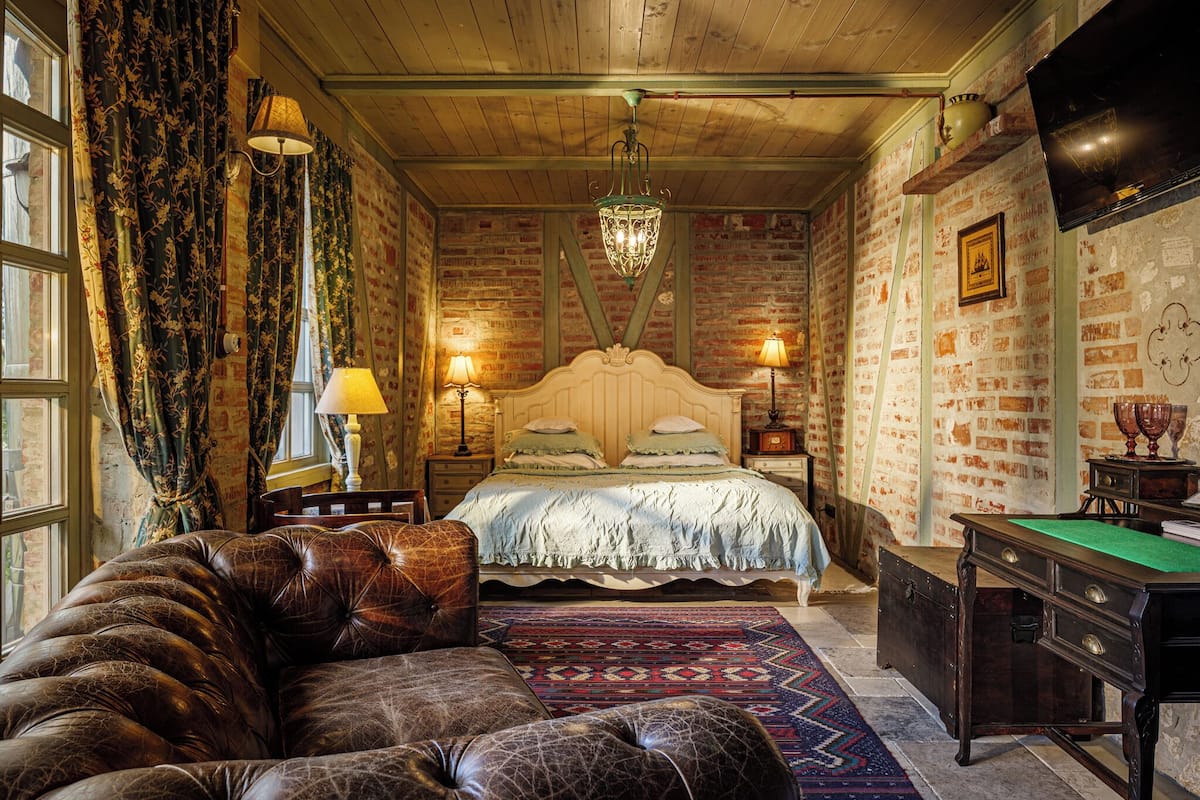 A cozy bedroom with a large bed, a leather sofa, a billiards table, and a brick wall.
