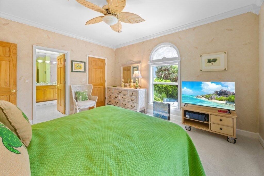 Un dormitorio con cama, cómoda, televisor y ventana con vistas a la vegetación.