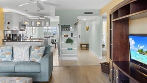A modern living room with a sofa, TV, and a kitchen in the background. - Sandpebble 3f 2 Bedroom Condo (Sanibel)