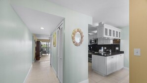 A modern kitchen with white cabinets, a black countertop, and a decorative wall piece. - Sandpebble 3f 2 Bedroom Condo (Sanibel)