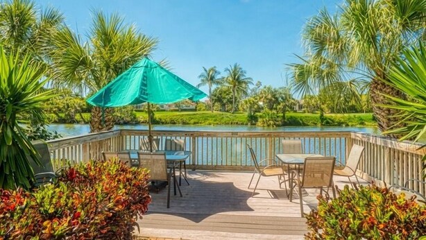 A wooden deck with outdoor furniture, a pool, and tropical vegetation. - Sandpebble 3f 2 Bedroom Condo (Sanibel)