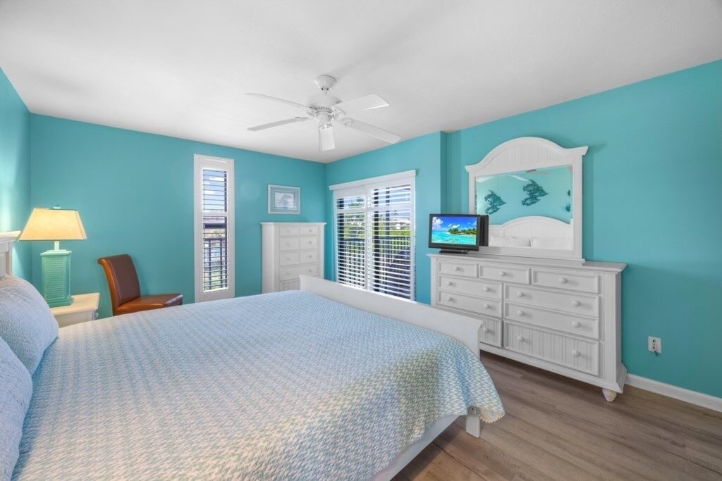Quarto com cama, cômoda, televisão e ventilador de teto.