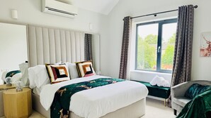 A bedroom with a large bed, a bedside table, a chair, a window with curtains, and an air conditioning unit. - Heliodor House in Cambridge (Cambridge)
