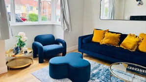 A modern living room with a blue sofa, matching ottoman, and a glass coffee table. - Heliodor House in Cambridge (Cambridge)