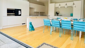 A modern kitchen with white cabinets, a built-in oven, and a dining area with blue chairs and a table set for four. - Heliodor House in Cambridge (Cambridge)