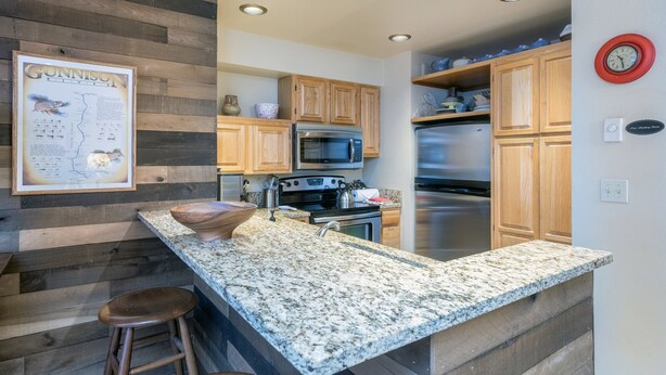 A kitchen with wooden cabinets, granite countertops, stainless steel appliances, and a framed map on the wall. - Alpine Escape 1 Bedroom Condo (Telluride)