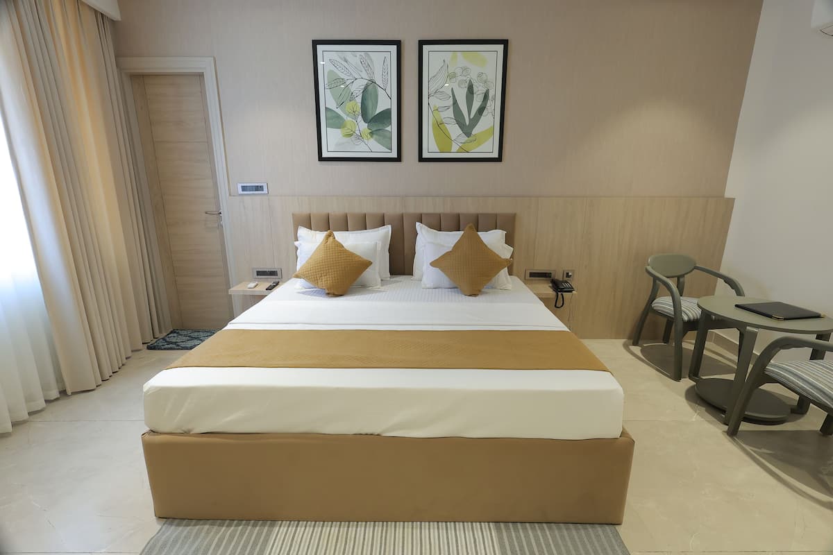 Une chambre d’hôtel avec un grand lit, deux oreillers, une table de chevet, une chaise et deux reproductions botaniques encadrées accrochées au mur.