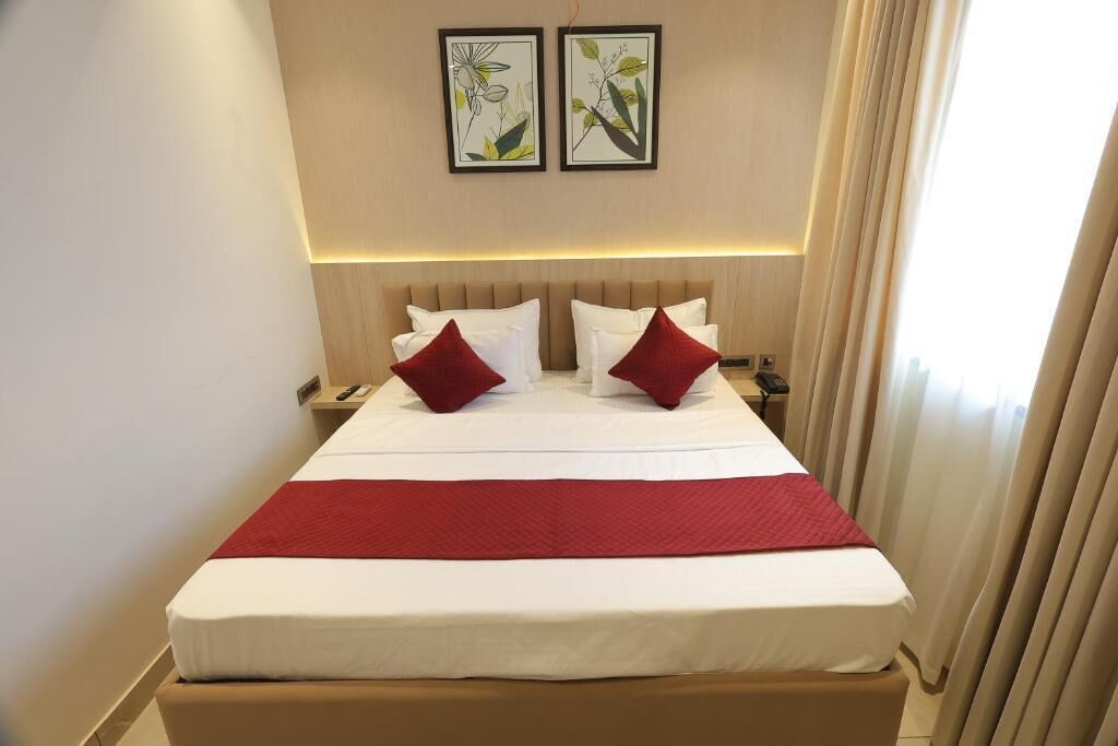 A hotel room with a large bed, two bedside tables, a red throw blanket, and two framed pictures on the wall.