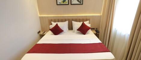 A hotel room with a large bed, two bedside tables, a red throw blanket, and two framed pictures on the wall.