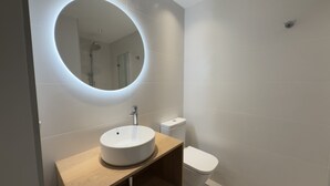 Un baño moderno con un espejo redondo, un lavabo e inodoro.