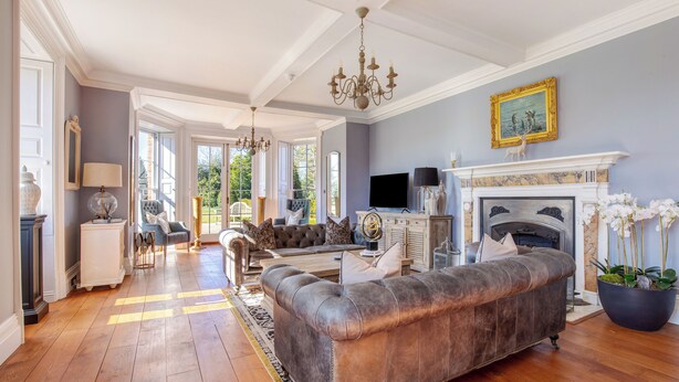 A spacious living room with a large leather sofa, a fireplace, and a chandelier.