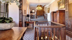 A grand staircase with a chandelier, wooden railings, and patterned floor tiles.