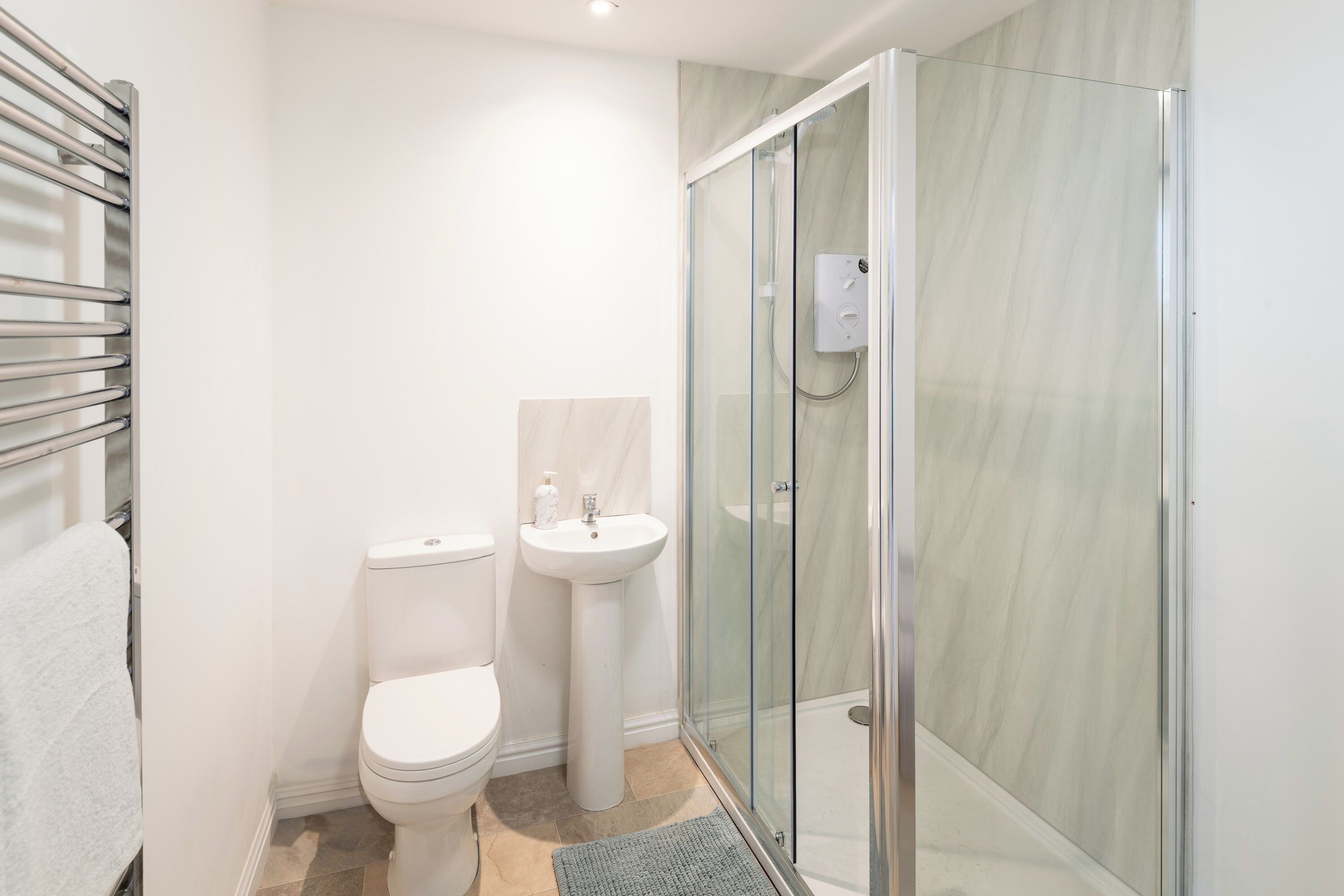 A modern bathroom with a toilet, pedestal sink, and a glass-enclosed shower.