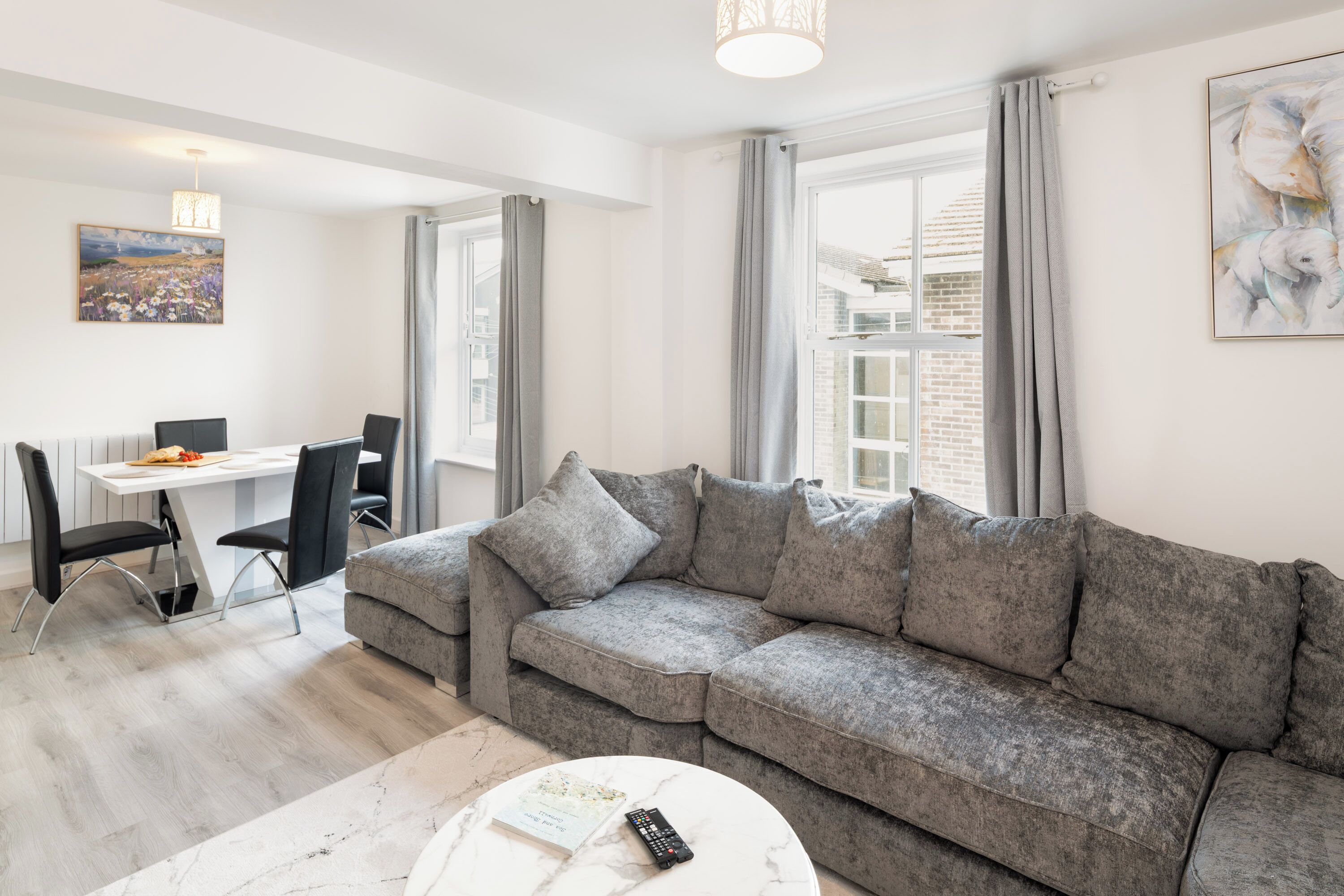 Un salon moderne avec un canapé gris, une table à manger avec des chaises et un tableau accroché au mur.