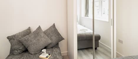 A modern bedroom with a grey sofa, a small bedside table, and a mirror.