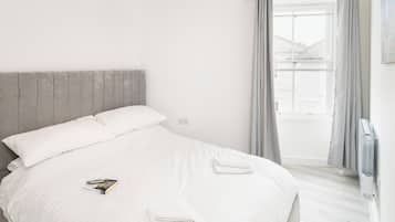 A neatly made bed with white linens, a book on the bed, and a folded towel.