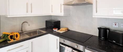 Eine moderne Küche mit weißen Schränken, einer Edelstahl-Spüle, einer schwarzen Arbeitsplatte, einem Toaster und einem Wasserkocher.