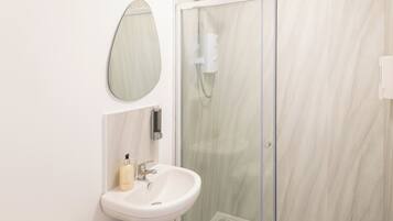 A modern bathroom with a glass-enclosed shower, a white sink, and a mirror.