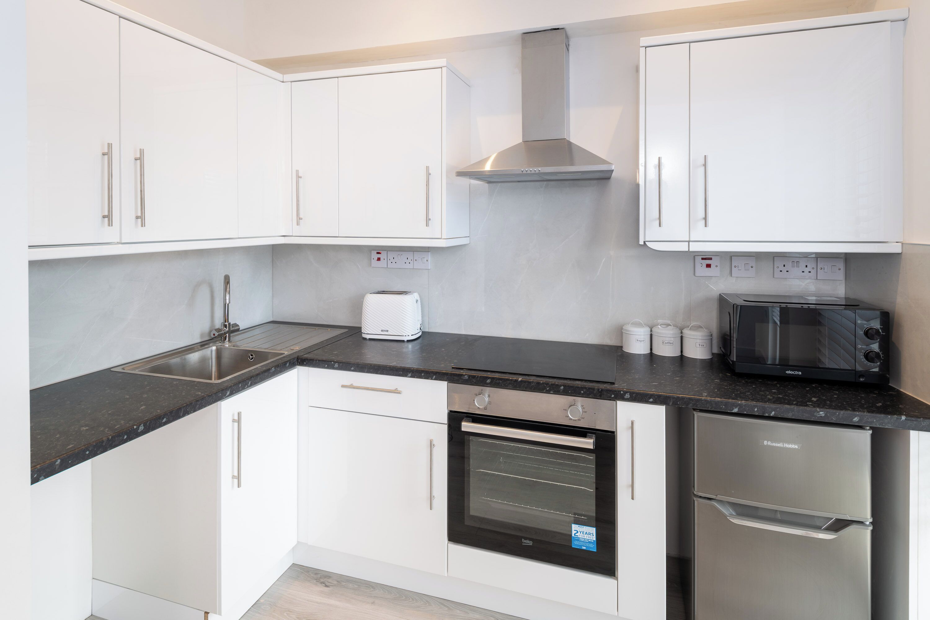 Een moderne keuken met witte kastjes, een roestvrijstalen afzuigkap, een inbouwoven, een magnetron en een broodrooster.