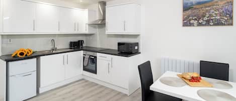 A modern kitchen with white cabinets, a black countertop, and a dining area with a white table and black chairs.