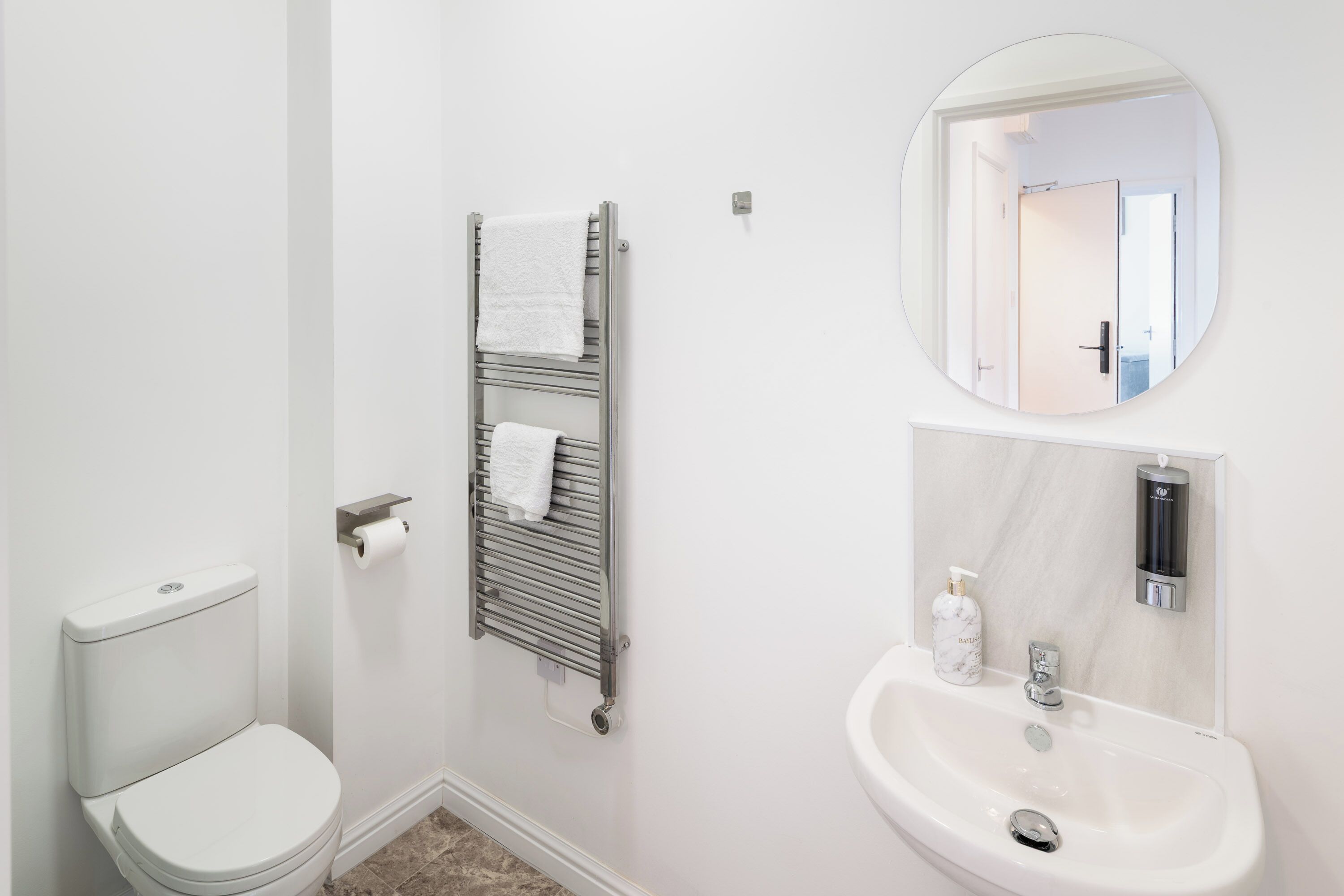 A modern bathroom with a toilet, a towel rack, a sink, and a mirror.
