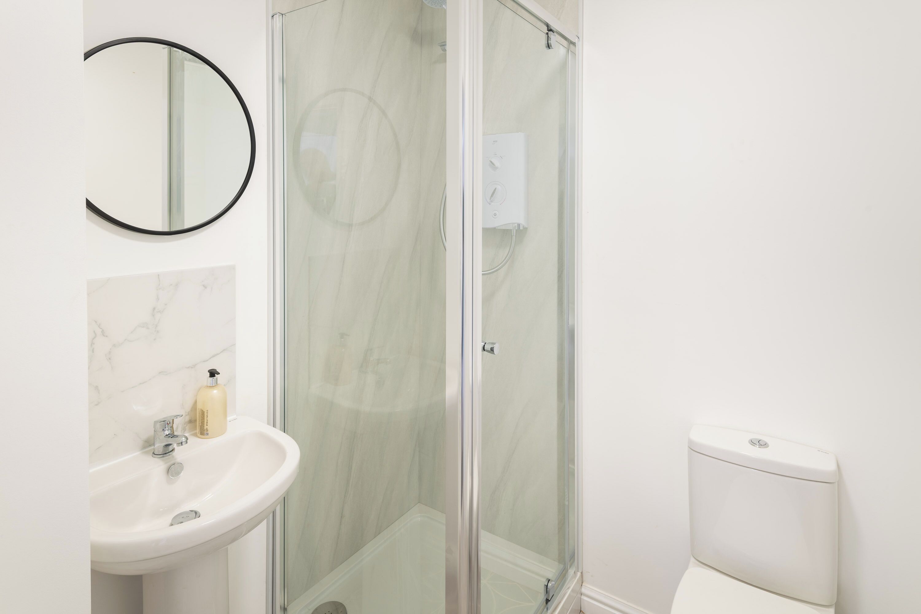 Een badkamer met een douchecabine van glas, een witte wastafel met een marmeren achterwand, en een toilet.